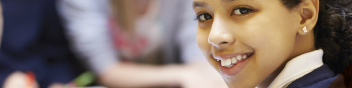 young girl turned to the camera smiling, with a blurred background behind her