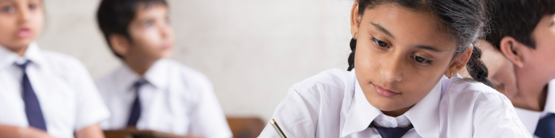 close up of girl writing, with other students blurred in the background