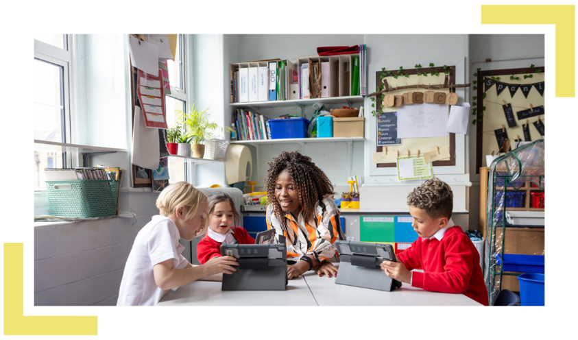Teacher in a classroom looking at a tablet with primary school aged pupils